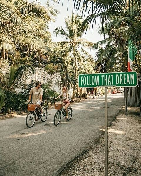 Couple biking down a palm-lined Tulum street
